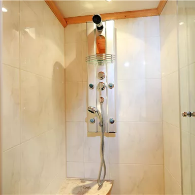 A modern shower with smooth, bright tiles and an elegant shower column. The shower is well-lit and looks inviting.