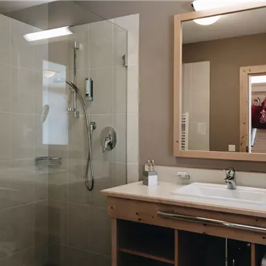 A modern bathroom with a shower and a large mirror. The walls are in neutral colors and there are wooden details.