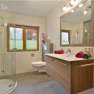 A modern bathroom with a shower cabin and a large mirror. The walls are in neutral tones and there are bright towels on the shelf.