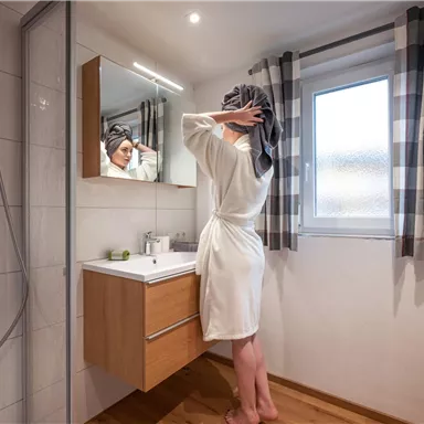 A modern bathroom view with a person in a bathrobe looking at themselves in the mirror. Bright colors and plenty of natural light create a pleasant atmosphere.