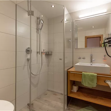 A modern bathroom with a enclosed shower and a clear mirror. The wooden shelf provides space for towels and toiletries.