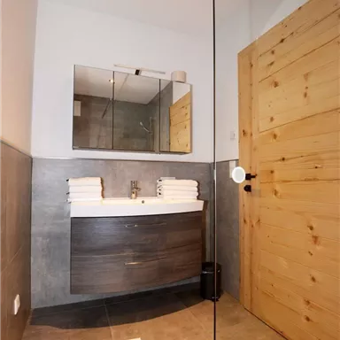A modern bathroom with a stylish sink and fresh towels. The walls are painted in neutral tones, and the wooden details add warmth.