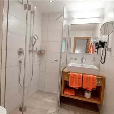 A modern bathroom with a shower, sink, and towel. Orange towels provide a fresh accent.