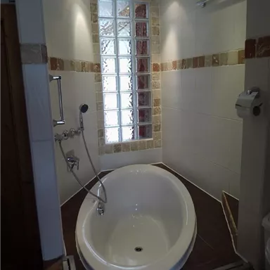 Ein modernes Badezimmer mit einer freistehenden Badewanne und einem gläsernen Wandabschnitt. Die Wände sind hell gefliest, und es gibt helle Beleuchtung.