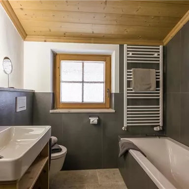 Ein modernes Badezimmer mit einer Badewanne und einem Waschbecken. Es hat eine Holzdecke und ausreichend Tageslicht durch das Fenster.