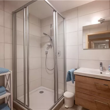 A modern bathroom with a shower and a sink. The walls are bright tiled and there are fresh towels in blue colors.