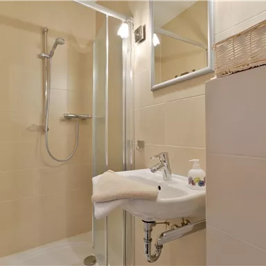 A modern bathroom with a shower cabin and a sink. The walls are painted in a light beige, giving a clean impression.