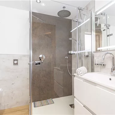 A modern bathroom with a glass shower and elegant fixtures. Bright walls and a wooden floor create an inviting atmosphere.