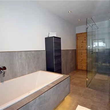 A modern bathroom with a bathtub and a glass shower. The walls are in a neutral color tone, and the furnishings are simple and stylish.