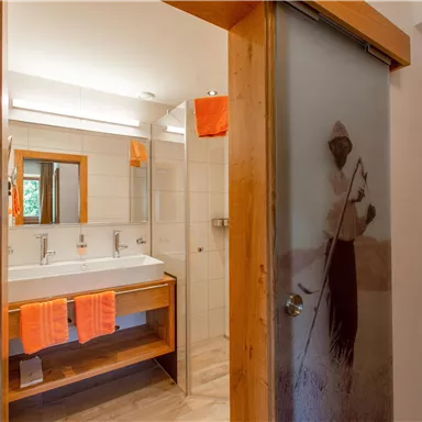 A modern bathroom with double washbasins and wooden details. Orange towels are stylishly hanging on the wall.