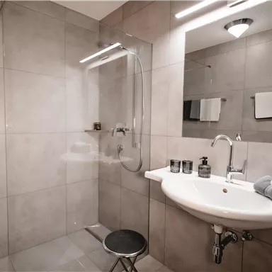 A modern bathroom with gray tiles and a walk-in shower. A sink with towels and toiletries completes the picture.