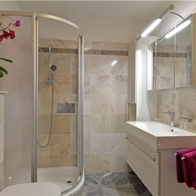 A modern bathroom with a shower and an elegant sink. Decorative flowers and a towel add a stylish touch to the space.