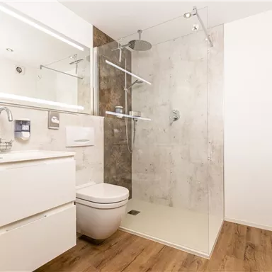 A modern bathroom with a glass shower cabin and an elegant sink. Bright walls and a wooden floor create a friendly atmosphere.