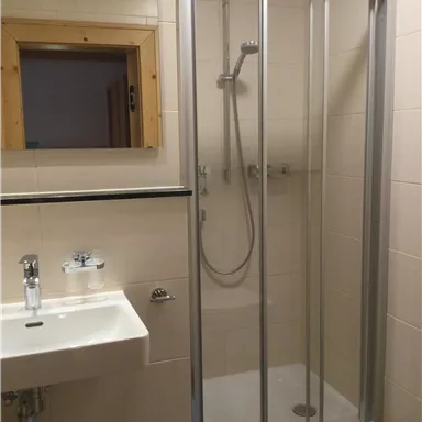 A modern bathroom with a shower and a sink. The walls are tiled in light colors and there is a window.