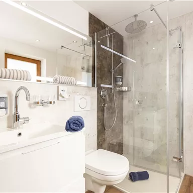 A modern bathroom with a shower and a sink. The walls are in neutral tones and there are towels in different colors.