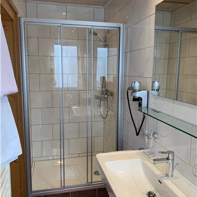 A modern bathroom with a shower cabin and a sink. The walls are decorated with tiles and there is a large mirror surface.
