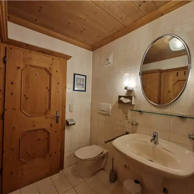 A bright bathroom with a wooden door and an oval mirror. The walls are tiled, and the furnishings are practical and modern.