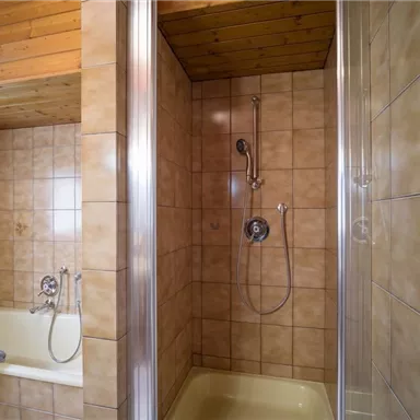 Ein Badezimmer mit einer Badewanne und einer Dusche. Die Wände sind gefliest und die Decke besteht aus Holz.