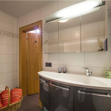Ein modernes Badezimmer mit einem abgerundeten Waschbecken und einem großen Spiegel. Auf der linken Seite liegt ein Korb mit Handtüchern.