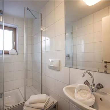 A modern bathroom with a glass shower and a vanity. It is bright and minimally designed, with white tiles and a large mirror.