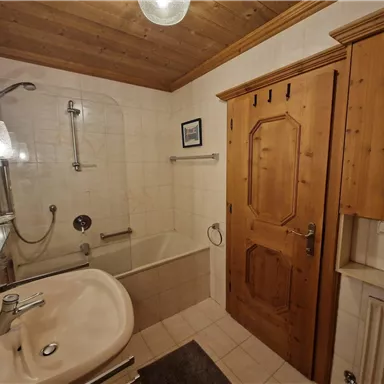 A modern bathroom with a bathtub and a shower cabin. The walls are light tiled and there are wooden details in the ceiling area.
