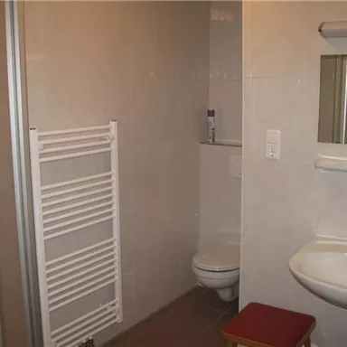 A modern bathroom with a shower, a sink, and a toilet. The walls are brightly tiled, and there is a towel holder.