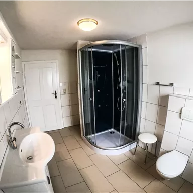 Ein modernes Badezimmer mit einer Duschkabine und hellen Fliesen. Es gibt ein Waschbecken, eine Toilette und eine Tür, die ins Freie führt.