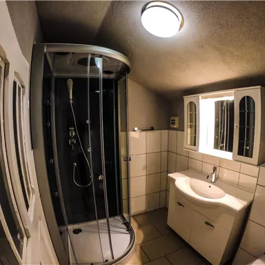 Ein modernes Badezimmer mit einer Dusche und einem Waschbecken. Das Licht ist hell und die Wände sind gefliest.