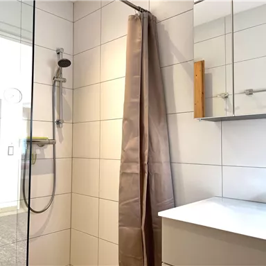 A modern bathroom with a shower and a large mirrored cabinet. The walls are tiled in light colors, and the room feels clean and inviting.