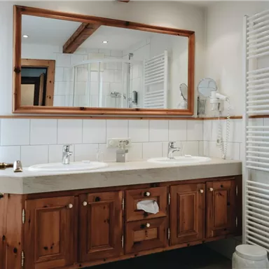 A modern bathroom with two sinks and wooden cabinets. There is a large mirror and bright tiled walls.
