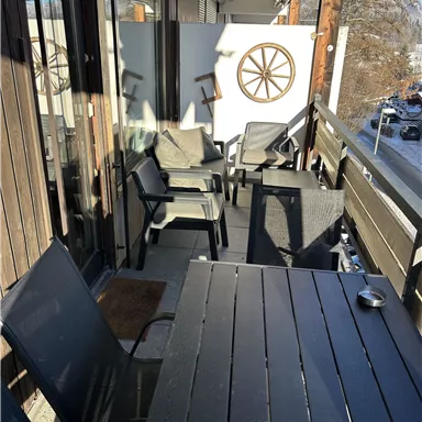 A cozy balcony with black furniture and a steering wheel on the wall. The space offers a view of the surroundings and invites relaxation.