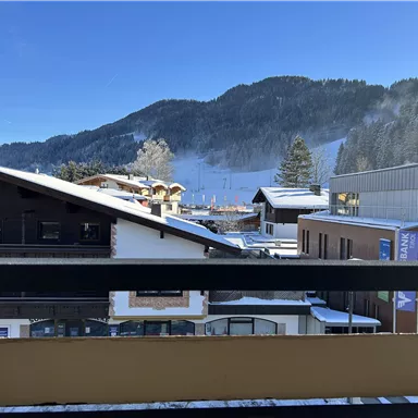 A winter landscape with snow-covered roofs and mountains in the background. The clear blue sky creates a fresh atmosphere.