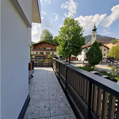 Ein Blick auf einen Balkon mit einem schönen Ausblick auf ein kleines Dorf. Im Hintergrund sind grüne Bäume und eine Kirchturm zu sehen.