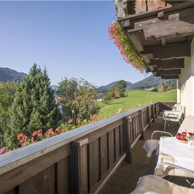Ein schöner Balkon mit Blick auf grüne Wiesen und Berge. Die Blumen und die Möbel laden zum Entspannen ein.