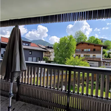Ein Balkon mit Blick auf grüne Bäume und ein hübsches Wohngebiet. Der Himmel ist klar mit einigen Wolken.