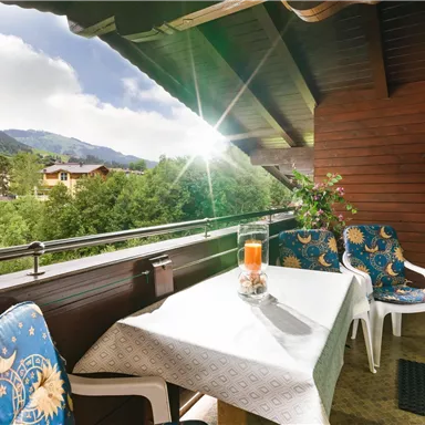 Ein schöner Balkon mit einem Tisch und zwei Stühlen. Im Hintergrund sind die Berge und die Natur gut sichtbar.