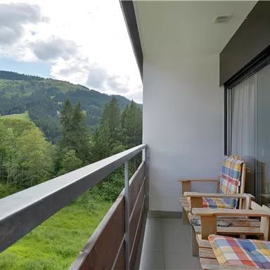 Ein Balkon mit zwei bequemen Stühlen und herrlichem Blick auf eine grüne Landschaft. Im Hintergrund sind Hügel und Bäume zu sehen.