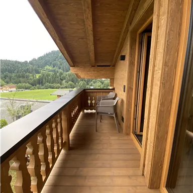 Ein Balkon mit Holzverkleidung und einem Blick auf die Berglandschaft. Darauf steht ein Stuhl und die Atmosphäre ist ruhig und einladend.