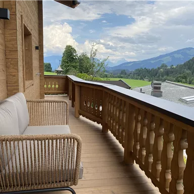 Ein gemütlicher Balkon mit einem Rattansofa und Blick auf grüne Berge. Die Atmosphäre ist entspannt und einladend.
