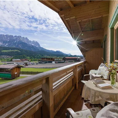 Ein Balkon mit Blick auf Berge und ein grünes Tal. Ein Tisch und zwei Stühle laden zum Entspannen ein.