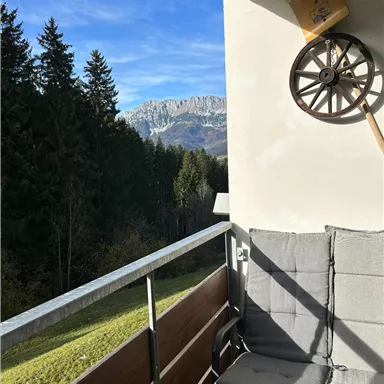 A balcony with two chairs and a beautiful view of mountains and trees. The sky is clear and the landscape is picturesque.