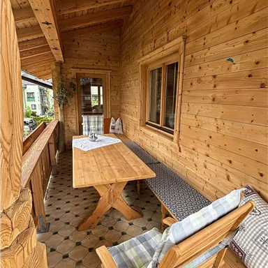 Eine gemütliche Veranda aus Holz mit einem großen Tisch und einer Bank. Der Raum ist einladend und perfekt für gesellige Zusammenkünfte.