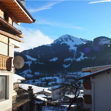 A picturesque mountain landscape with snow-capped peaks and a bright blue sky. In the foreground, traditional houses with wooden balconies can be seen.