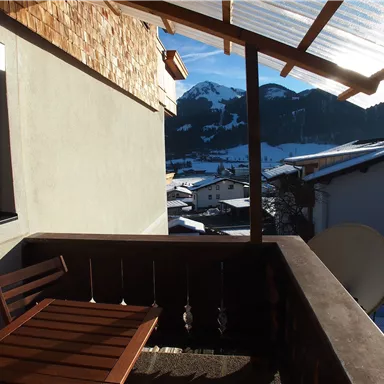 A balcony with a wooden table and a view of snow-covered mountains. The sun is shining, and the view is calm and picturesque.