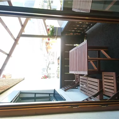 A balcony with a wooden terrace and a table. The view shows a bright room and some plants.