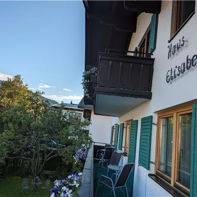 A charming house named "Haus Elisabeth" with green shutters.
In the foreground, there is a balcony overlooking a garden and the surrounding landscape.