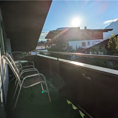 A balcony with several chairs and a view of the mountains. The sun is shining brightly and the sky is clear.