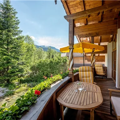 Ein schöner Balkon mit Holzdecke und komfortablen Sitzgelegenheiten. Der Blick fällt auf üppige Bäume und eine grüne Landschaft.