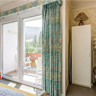 Ein helles Zimmer mit einem Balkonblick auf die Berge. Es gibt ein Etagenbett, einen Schrank und einen gemütlichen Sessel.