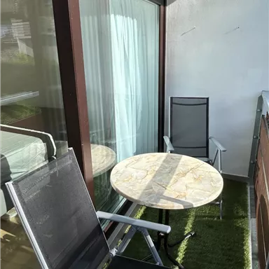 A small balcony with two chairs and a round table. The sun is shining on the furnished area.